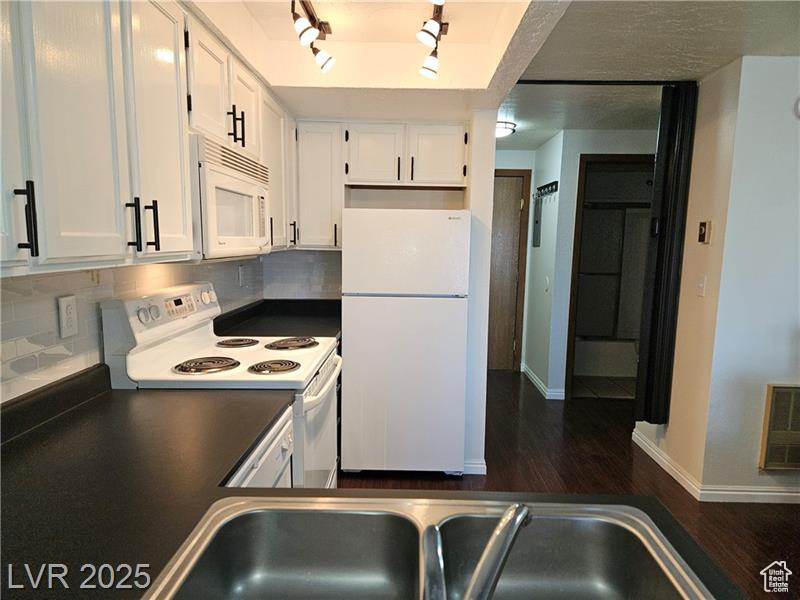 Kitchen featuring white appliances, dark countertops, white cabinets, and dark wood finished floors