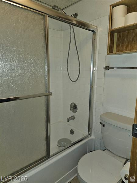Full bath featuring combined bath / shower with glass door and toilet