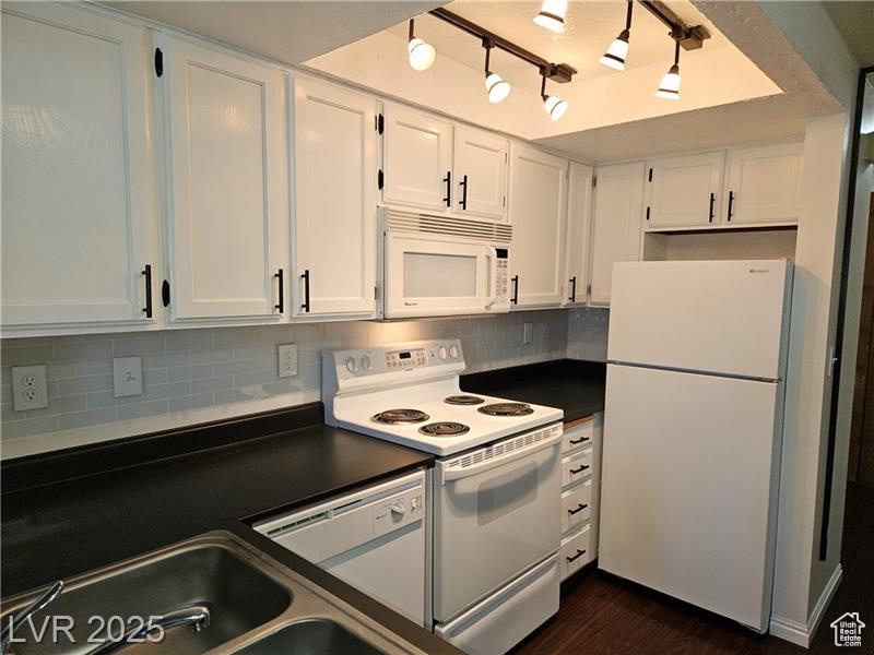 Kitchen featuring white appliances, dark countertops, white cabinetry, backsplash, and dark wood-style floors