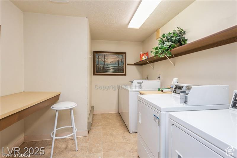 Communal laundry room with washing machine and dryer and light tile patterned flooring