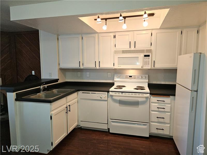 Kitchen featuring white appliances, dark countertops, white cabinets, and dark wood-style flooring