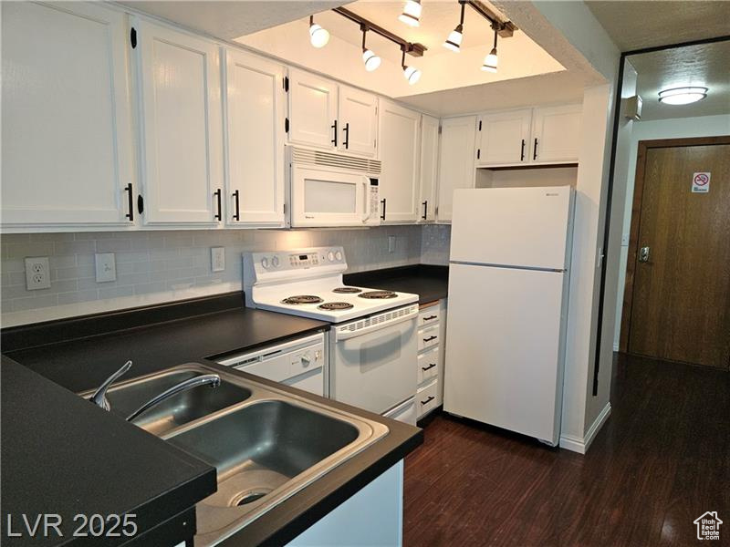 Kitchen with white appliances, dark countertops, white cabinetry, and dark wood-type flooring
