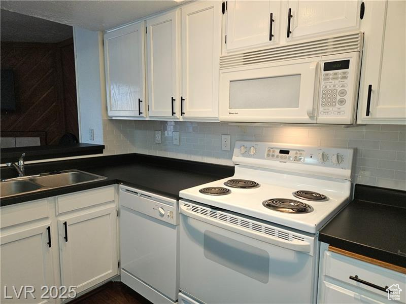 Kitchen featuring white appliances, dark countertops, white cabinetry, and decorative backsplash