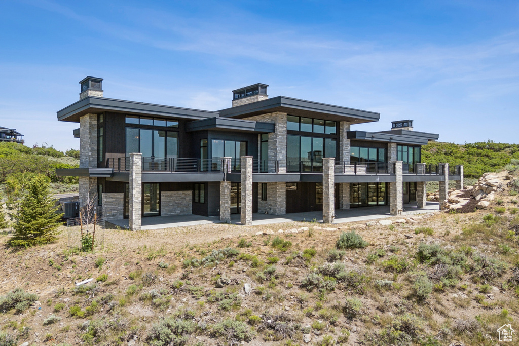 Rear view of property featuring stone siding, a patio area, and a balcony