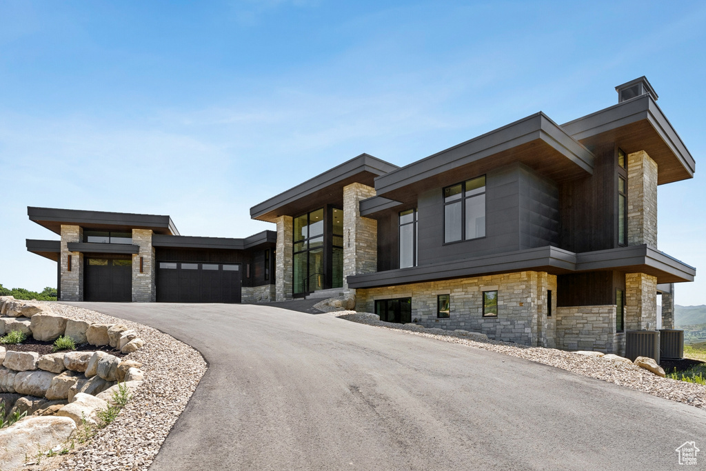 Contemporary house with stone siding, an attached garage, and driveway