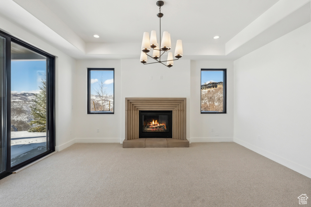 Unfurnished living room featuring a raised ceiling, carpet flooring, a chandelier, a glass covered fireplace, and recessed lighting