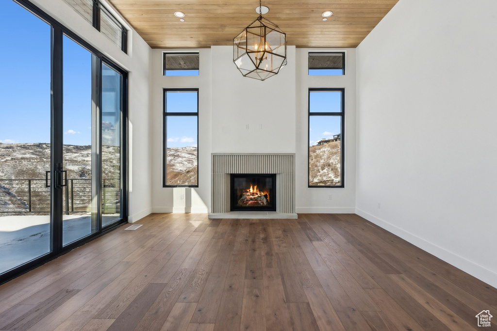 Unfurnished living room featuring healthy amount of natural light, a chandelier, wooden ceiling, hardwood / wood-style flooring, and a glass covered fireplace