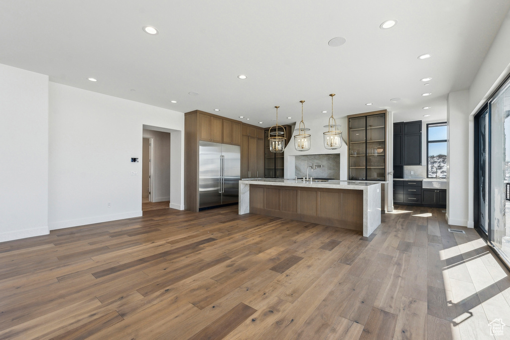 Kitchen featuring built in refrigerator, light countertops, wood finished floors, recessed lighting, and a spacious island