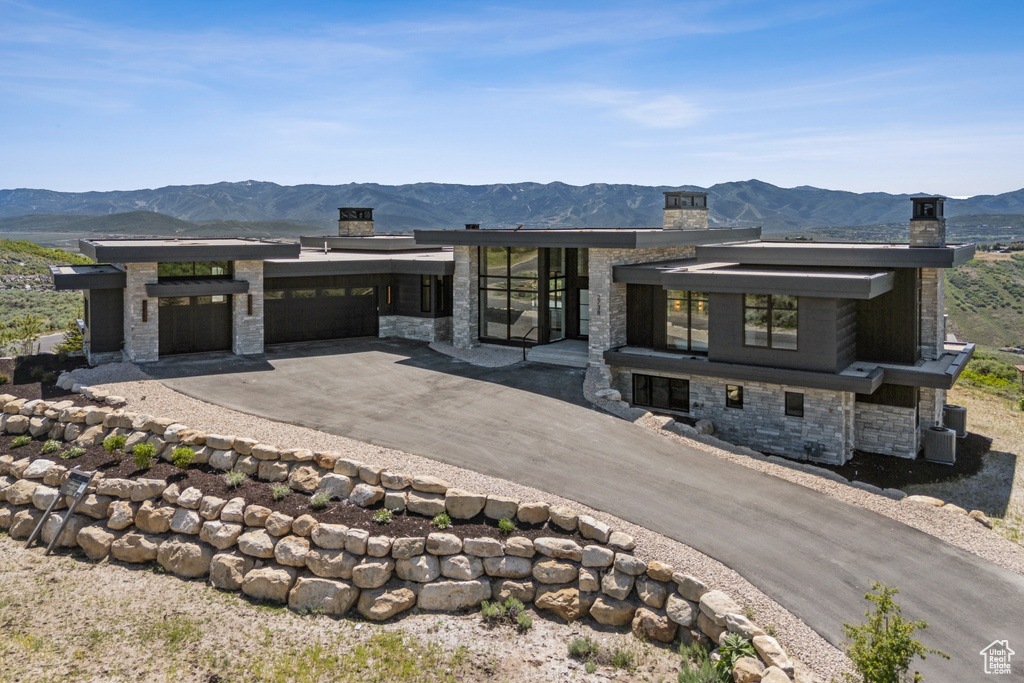 Contemporary house featuring stone siding, a chimney, a mountain view, and an attached garage