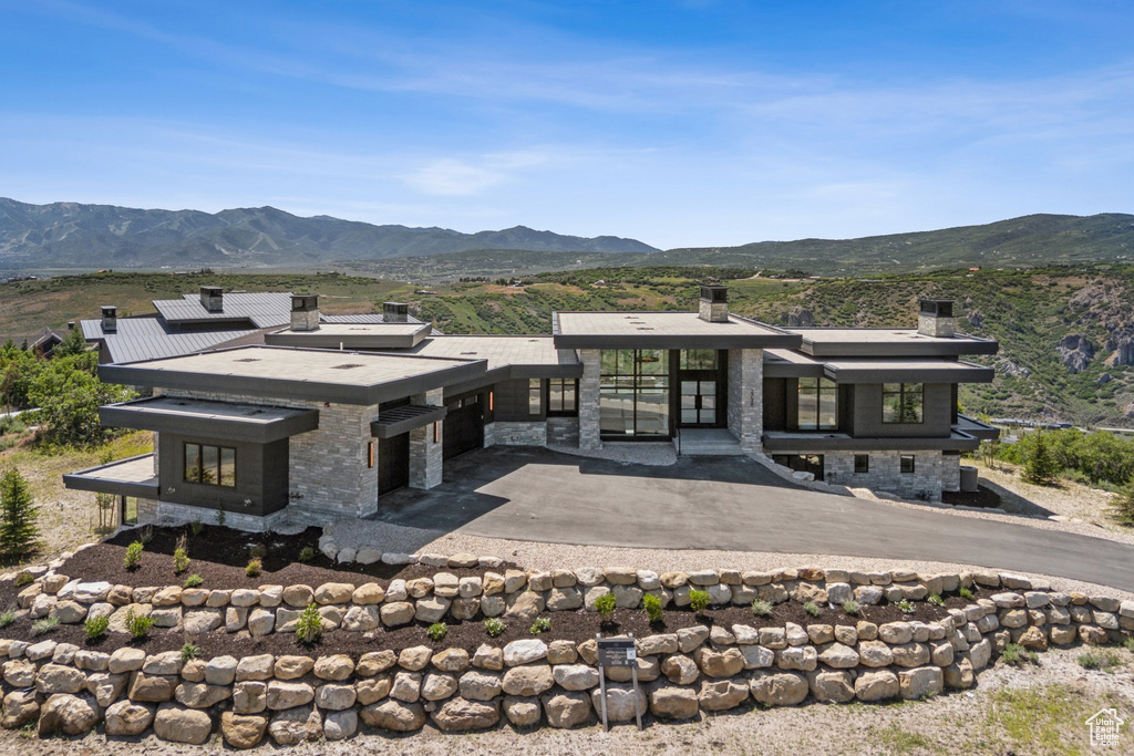 Back of house with a chimney, a mountain view, stone siding, and a garage
