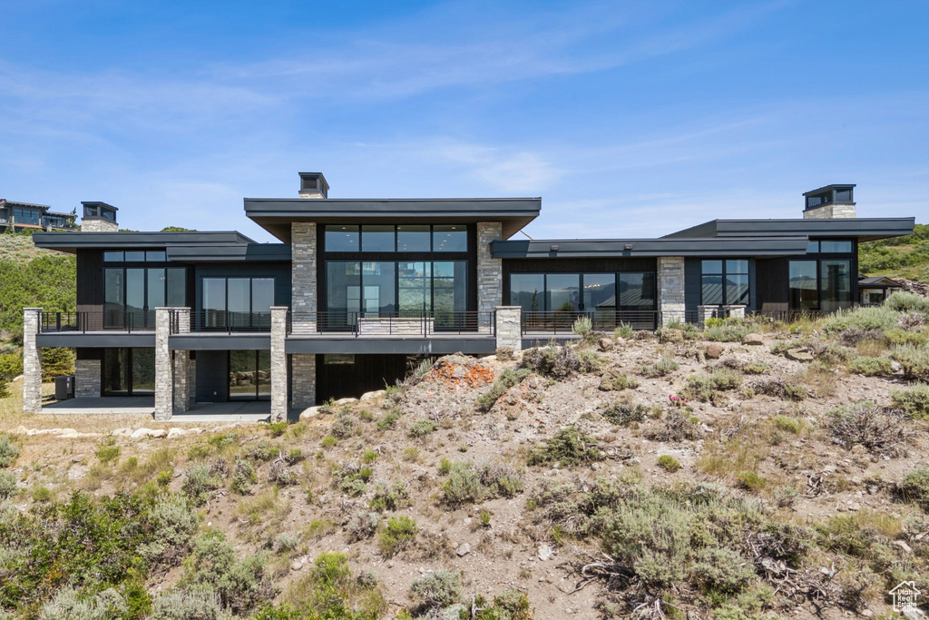 Back of property featuring stone siding and a balcony