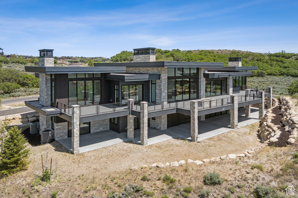 Back of property featuring stone siding, a chimney, a patio area, and a deck