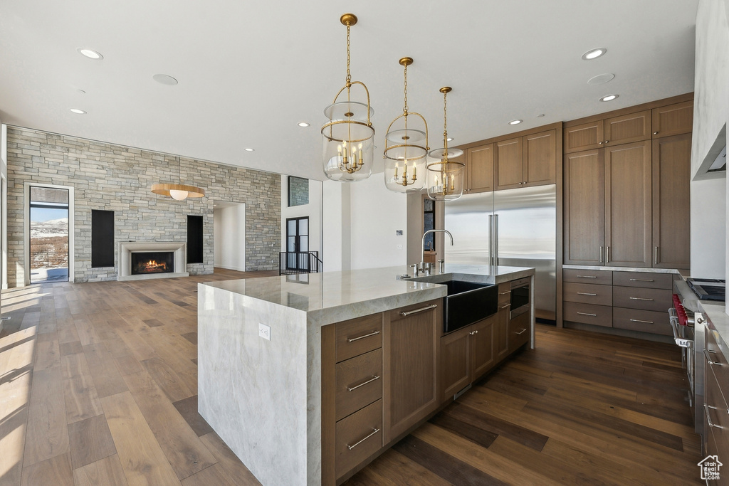 Kitchen featuring dark wood-type flooring, a kitchen island with sink, recessed lighting, light stone counters, and a chandelier