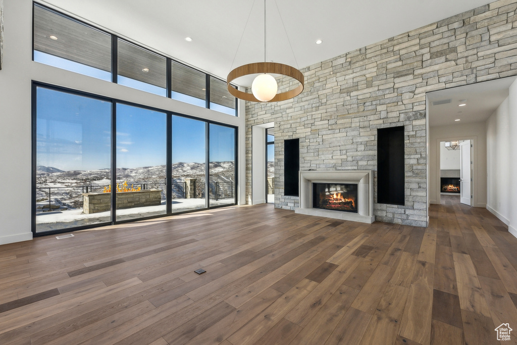 Unfurnished living room featuring a stone fireplace, a mountain view, a towering ceiling, hardwood / wood-style floors, and recessed lighting
