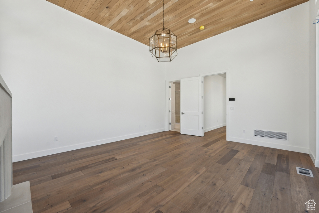 Unfurnished dining area with a chandelier, a high ceiling, wooden ceiling, and dark wood-style flooring