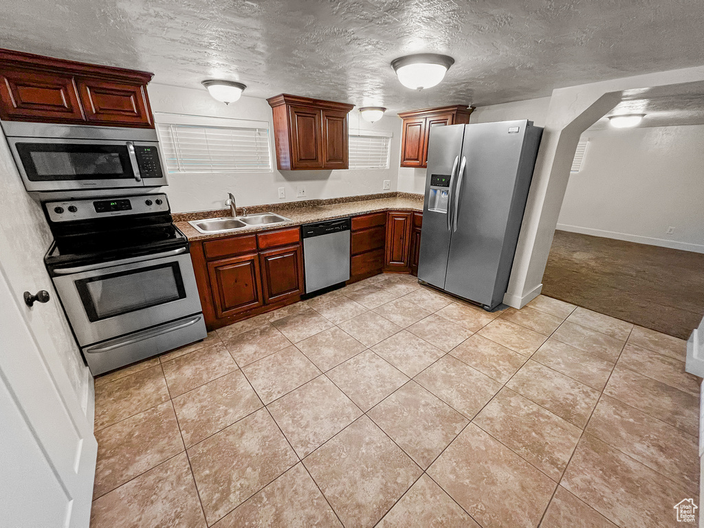 Kitchen with sink, light tile patterned floors, stainless steel appliances, and a textured ceiling