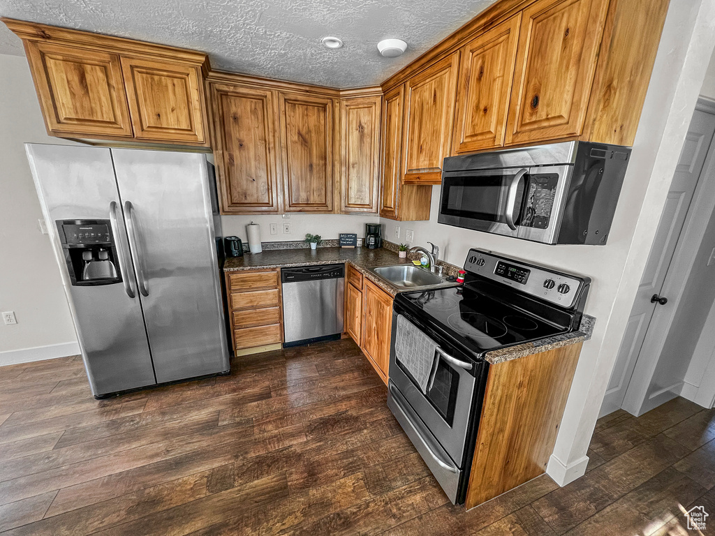 Kitchen with appliances with stainless steel finishes, dark hardwood / wood-style floors, sink, and a textured ceiling