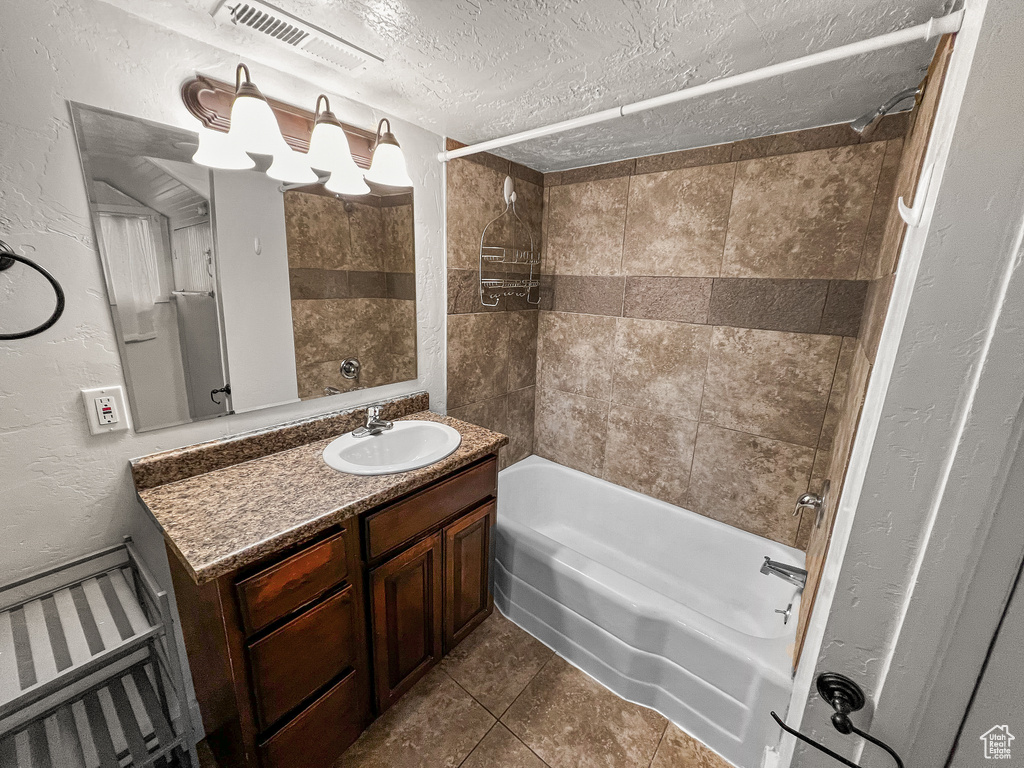 Bathroom featuring tile patterned floors, vanity, tiled shower / bath combo, and a textured ceiling