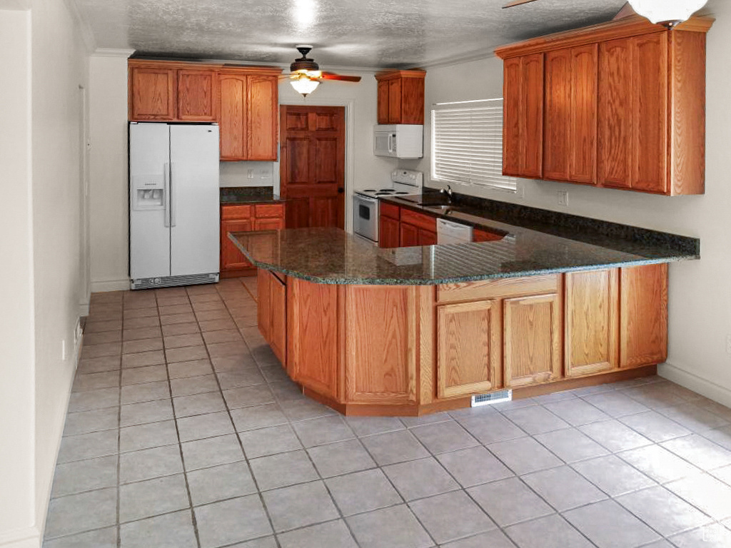 Kitchen with ceiling fan, white appliances, dark stone counters, and kitchen peninsula