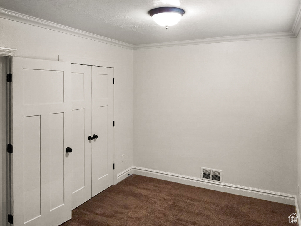 Unfurnished bedroom featuring dark carpet, ornamental molding, a closet, and a textured ceiling