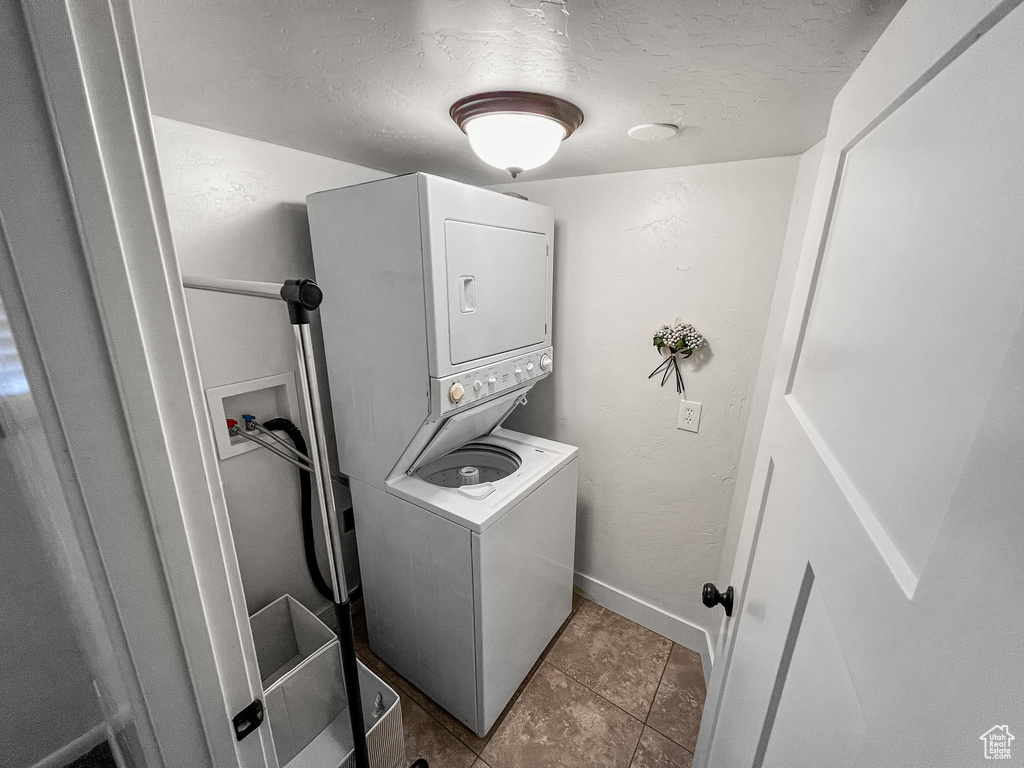Laundry room with stacked washer and dryer, light tile patterned flooring, and a textured ceiling