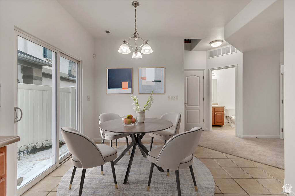 Dining space featuring light carpet, light tile patterned floors, baseboards, visible vents, and an inviting chandelier