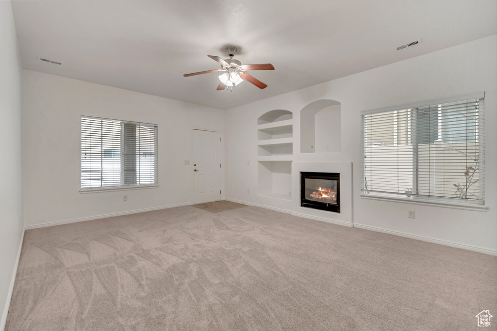 Unfurnished living room with ceiling fan, light carpet, and built in features