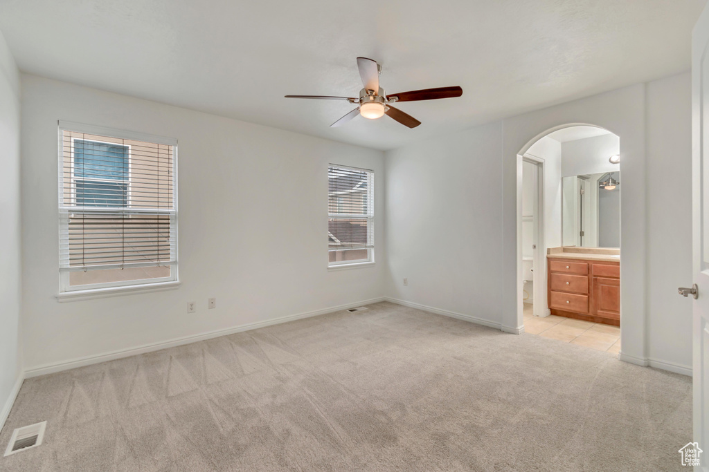 Unfurnished bedroom featuring connected bathroom, light colored carpet, and ceiling fan