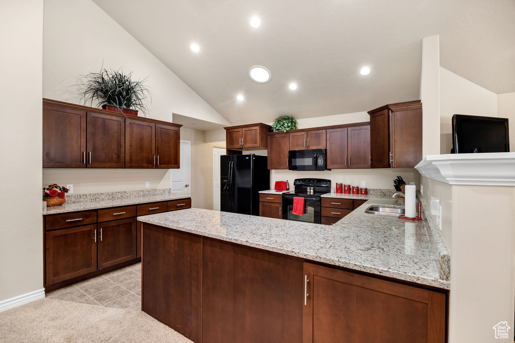 Kitchen with lofted ceiling, sink, light stone counters, black appliances, and kitchen peninsula