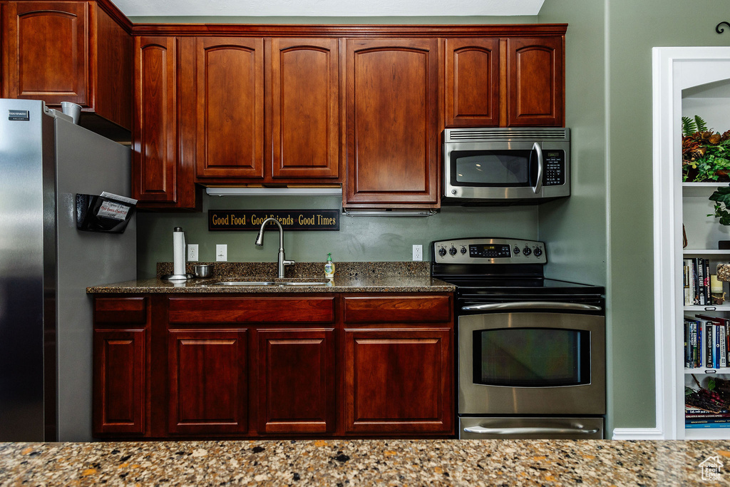 Kitchen with light stone counters, stainless steel appliances, and sink