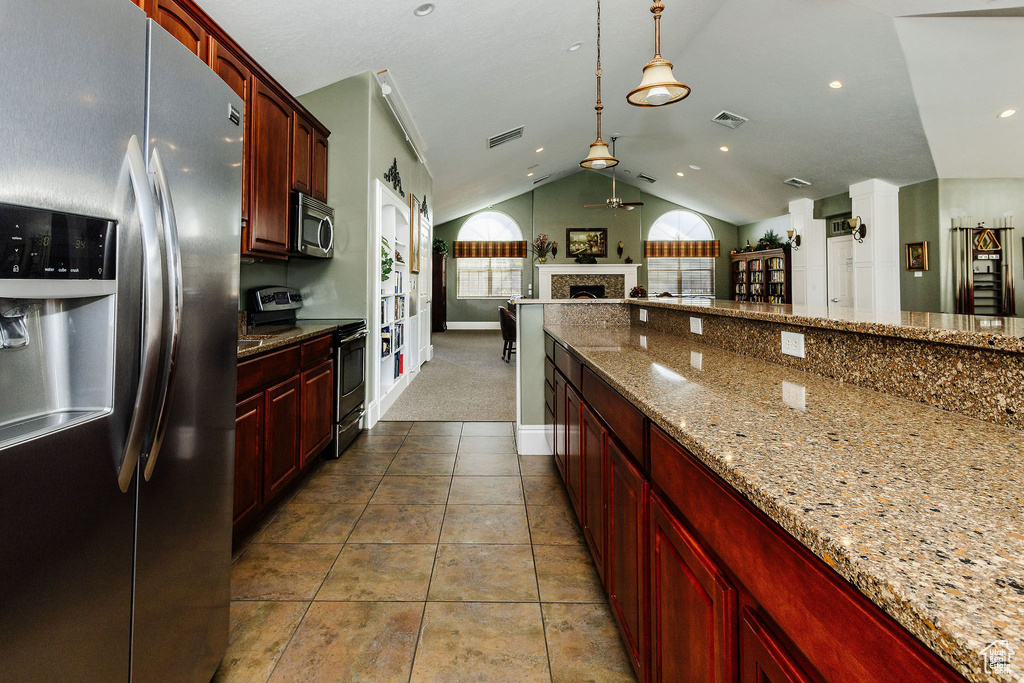 Kitchen featuring appliances with stainless steel finishes, tile patterned flooring, hanging light fixtures, light stone counters, and vaulted ceiling