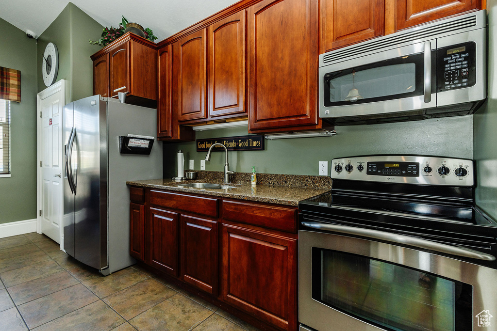 Kitchen featuring stainless steel appliances, sink, dark stone countertops, and light tile patterned floors