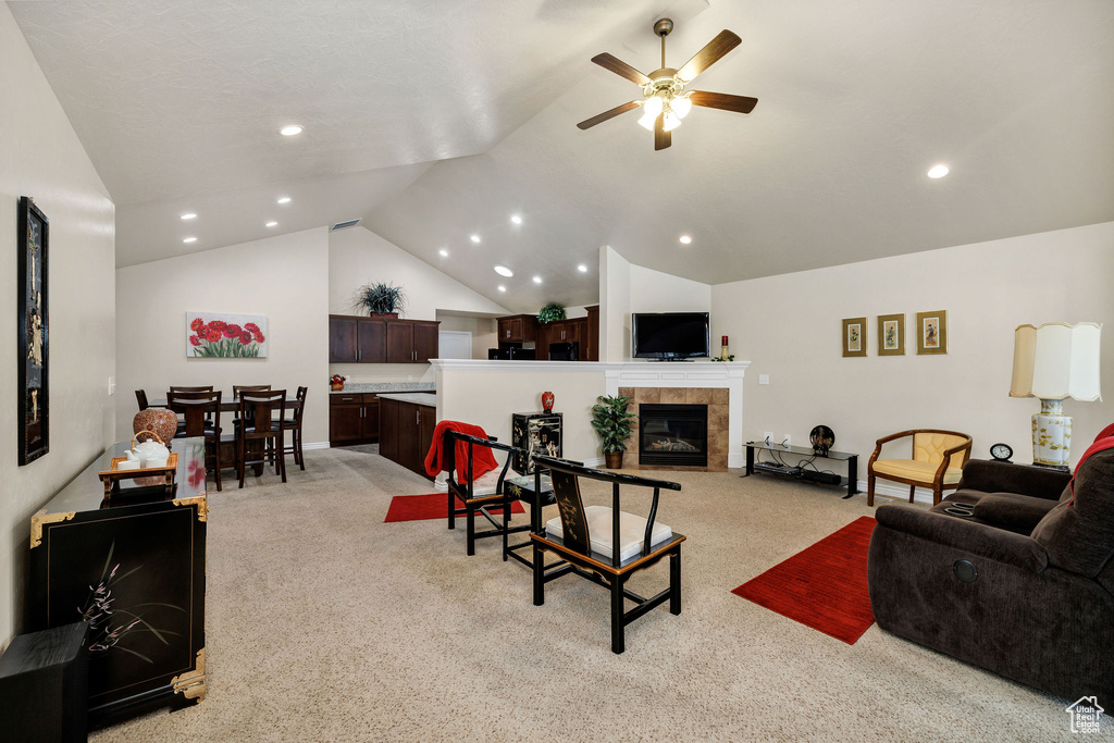 Living room with a tiled fireplace, vaulted ceiling, light colored carpet, and ceiling fan