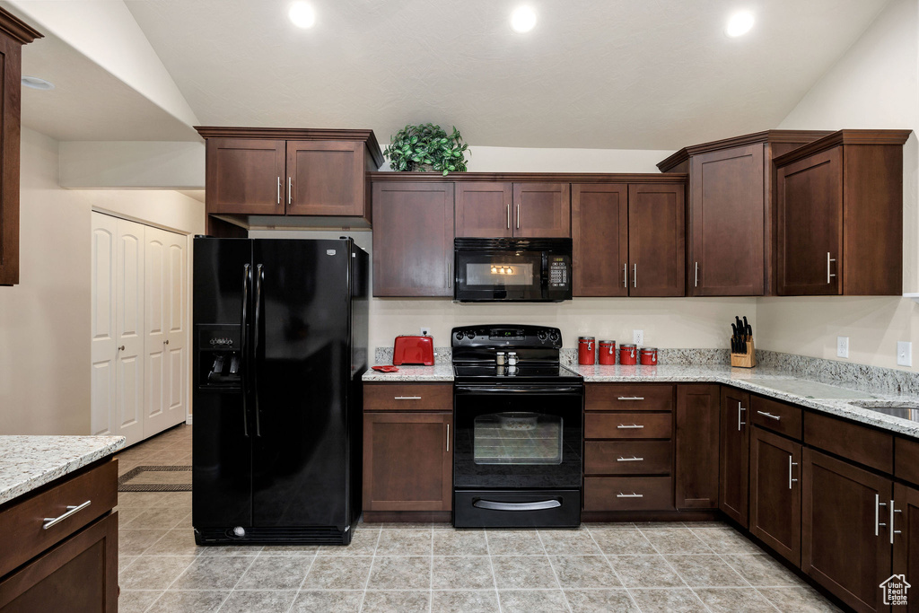 Kitchen featuring light stone counters, lofted ceiling, dark brown cabinets, and black appliances