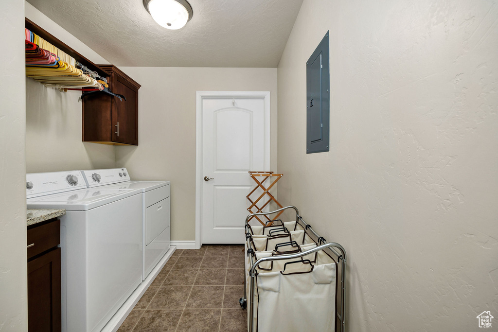 Clothes washing area with washer and clothes dryer, electric panel, cabinets, a textured ceiling, and dark tile patterned flooring