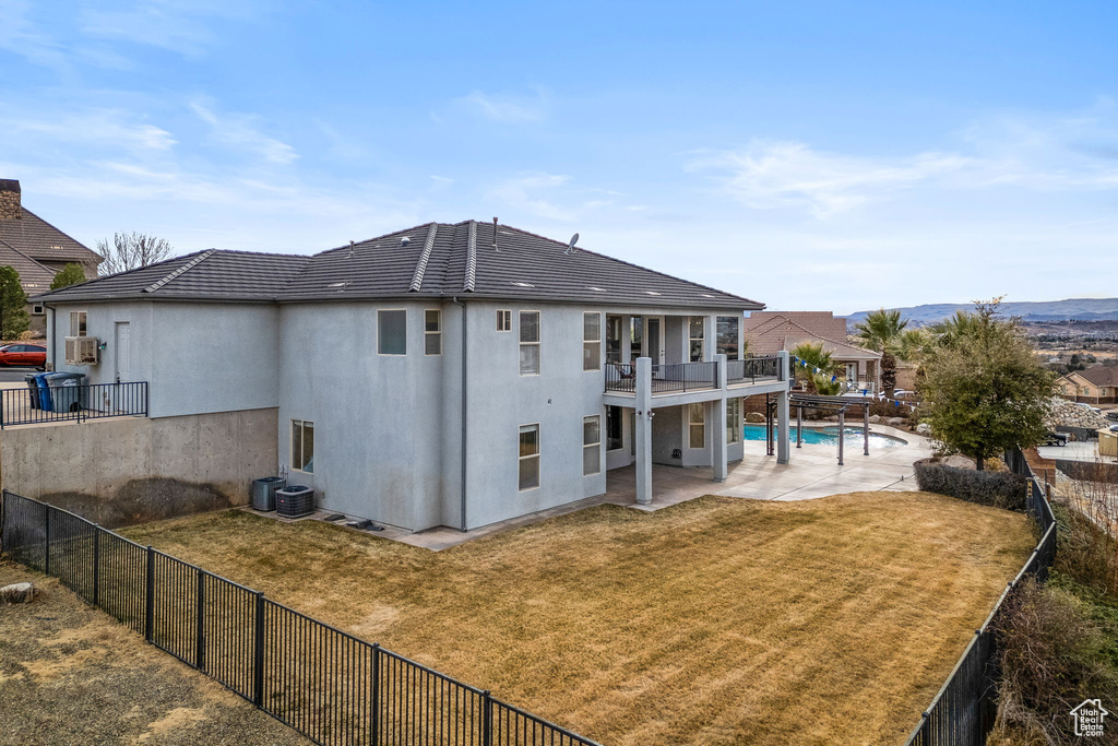 Rear view of property featuring a fenced in pool, a lawn, a patio area, and a balcony
