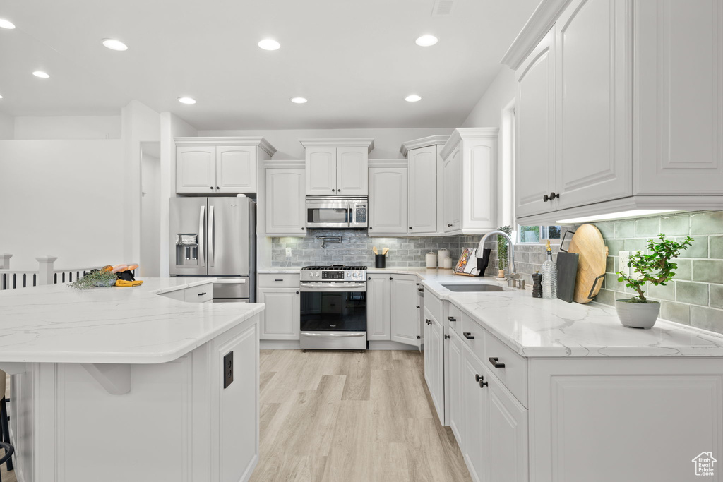 Kitchen with sink, a breakfast bar area, white cabinetry, stainless steel appliances, and a kitchen island