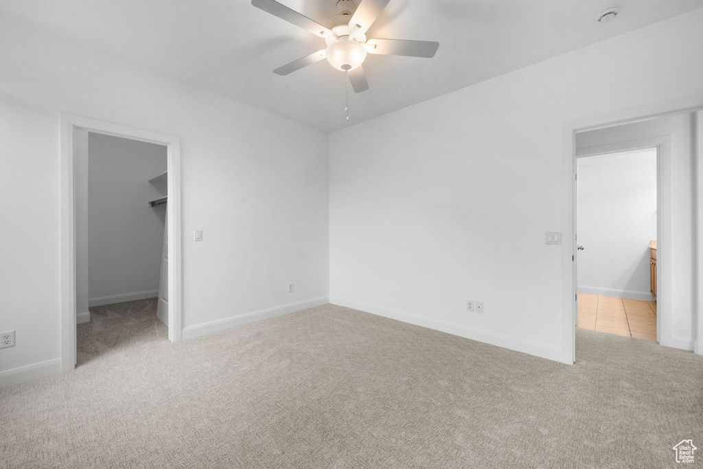 Unfurnished bedroom with light carpet, a spacious closet, a closet, and ceiling fan