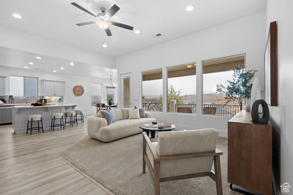 Living room with ceiling fan with notable chandelier and light hardwood / wood-style floors