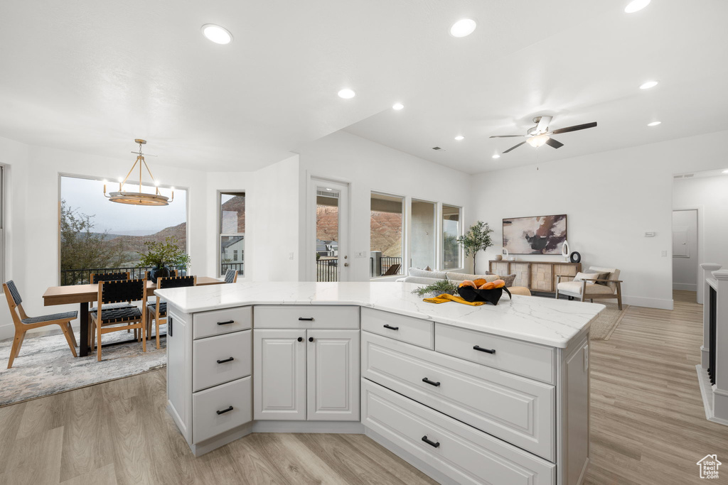 Kitchen featuring light stone countertops, white cabinets, light hardwood / wood-style floors, and decorative light fixtures