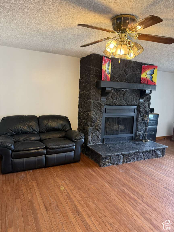 Living room with a textured ceiling, wood finished floors, a fireplace, and a ceiling fan