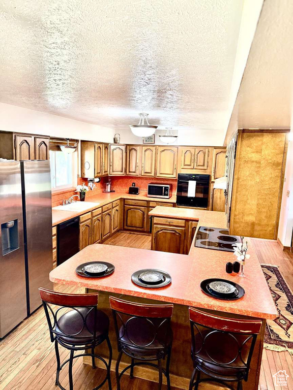Kitchen featuring black appliances, a textured ceiling, light wood-style flooring, light countertops, and a peninsula