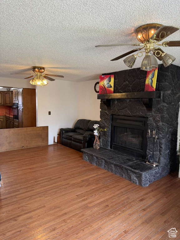 Living room featuring a ceiling fan, light wood-type flooring, a fireplace, and a textured ceiling