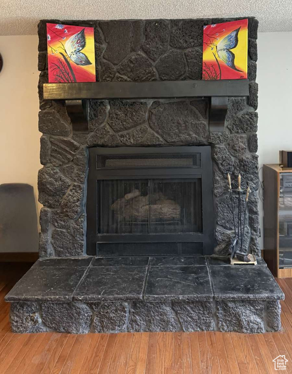 Detailed view of a stone fireplace, a textured ceiling, and wood finished floors