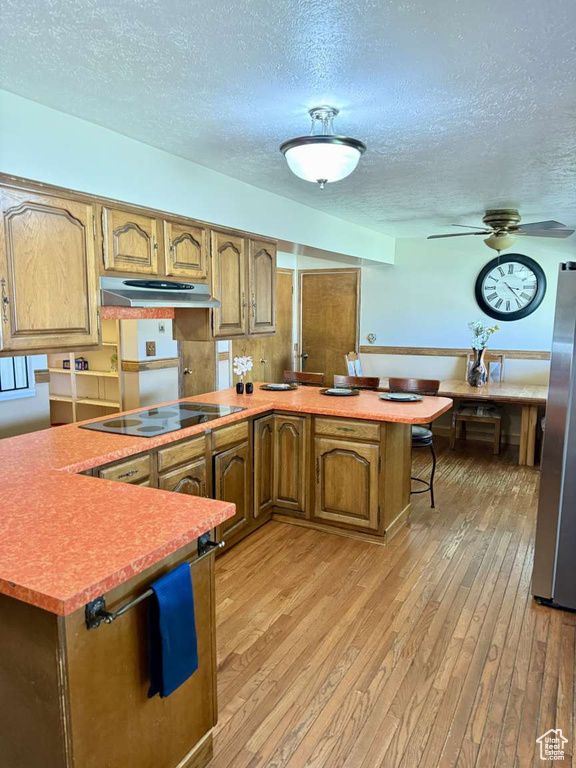 Kitchen with a peninsula, black electric cooktop, under cabinet range hood, light wood finished floors, and a textured ceiling