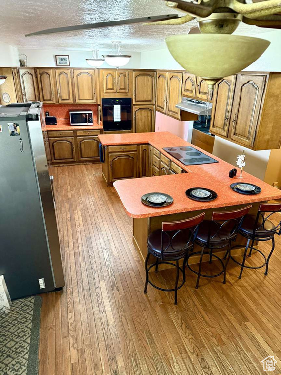 Kitchen with black appliances, hardwood / wood-style floors, a kitchen island, brown cabinets, and light countertops