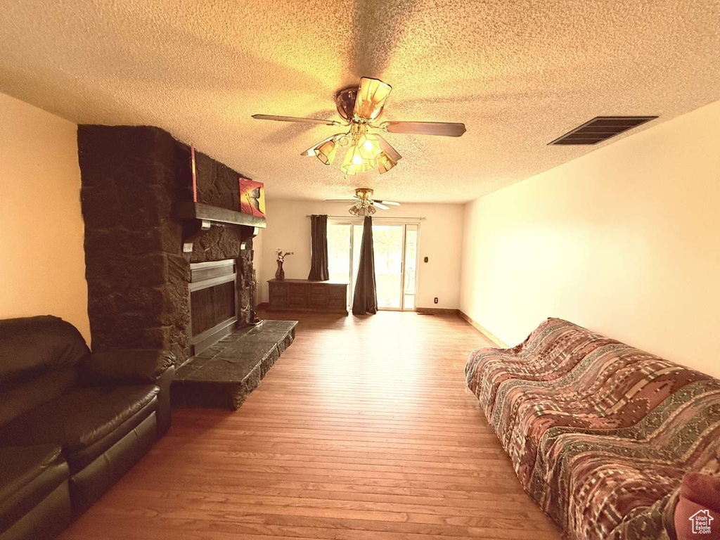 Living room featuring a textured ceiling, hardwood / wood-style floors, ceiling fan, and a fireplace