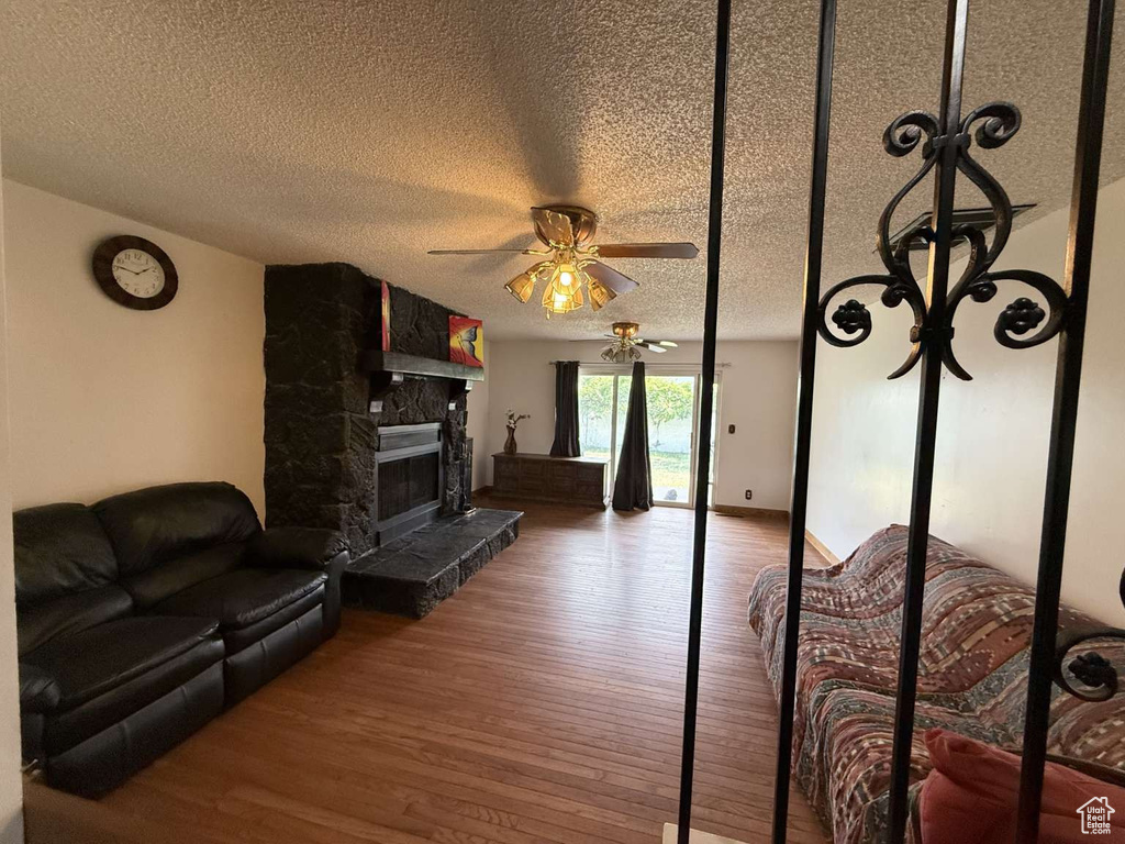 Living room with a ceiling fan, wood finished floors, a textured ceiling, and a stone fireplace