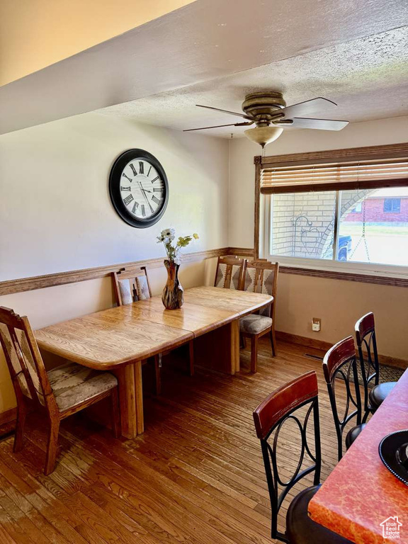 Dining area with a ceiling fan, wood-type flooring, a textured ceiling, and baseboards