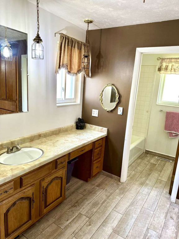 Bathroom featuring wood finished floors, vanity, a textured ceiling, shower / bath combination, and baseboards
